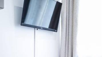 Ein rotes Sofa mit zwei gelben Kissen, ein flachbildfernseher an der Wand und ein Fenster mit Vorhängen.