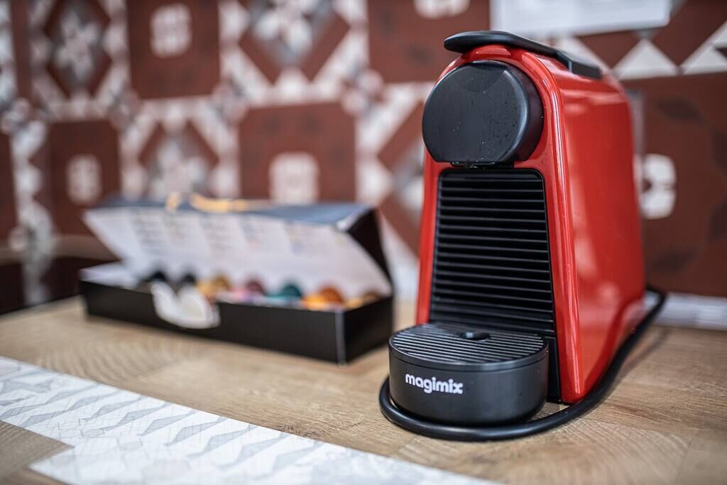 Une machine à café rouge, avec une base noire, posée sur une table en bois.