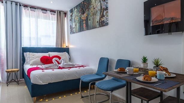 A hotel room with a bed, a dining table with breakfast, a TV, and a painting on the wall. - Beautiful Break in Paris Gentilly (Gentilly)