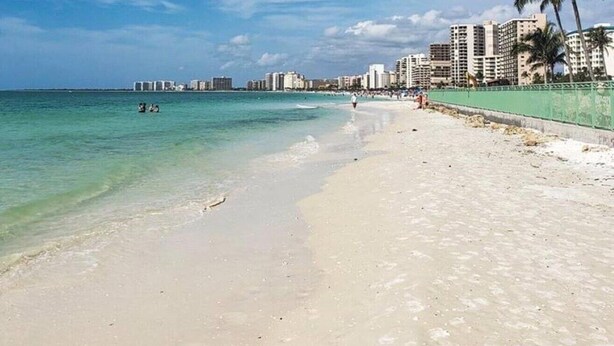 A beach with clear turquoise water, a sandy shore, and a cityscape in the background. - Marco Beach Haven 2 blocks from South Beach! (Marco Island)