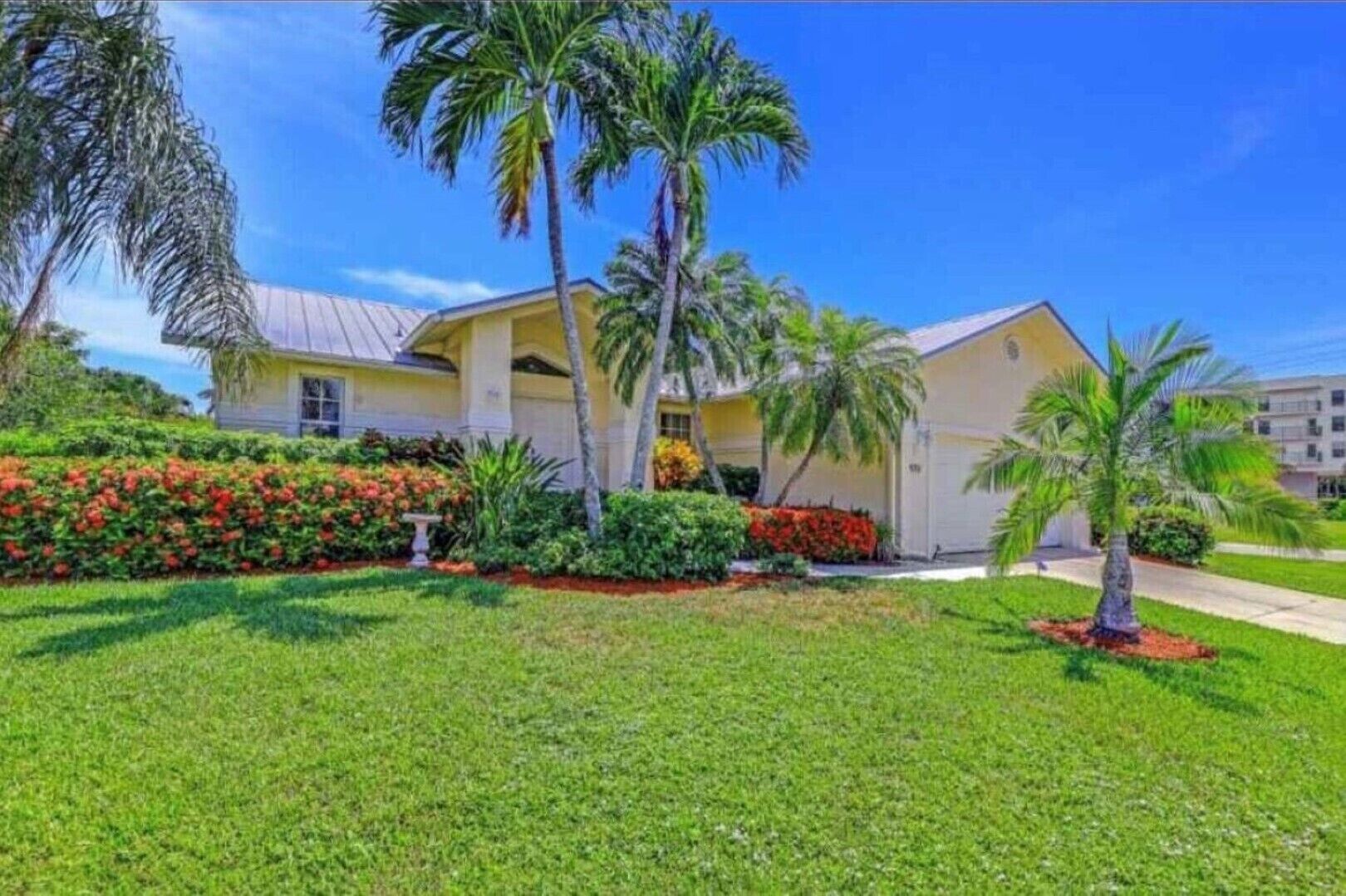 A two-story building with a yellow facade, surrounded by well-maintained gardens and palm trees.