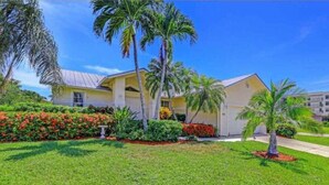 A two-story building with a yellow facade, surrounded by well-maintained gardens and palm trees. - Marco Beach Haven 2 blocks from South Beach! (Marco Island)