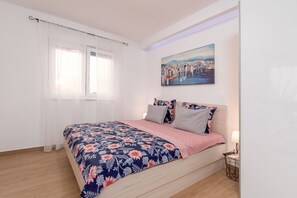 Ein Schlafzimmer mit einem Bett, einem Bild, einem Fenster mit Vorhängen und einem Nachttisch mit einer Lampe.