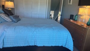 Een slaapkamer met een bed, een dressoir, een kledingkast en een televisie aan de muur.