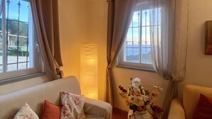 Een woonkamer met een beige bank, een kleinere fauteuil en een bloemenvaas.