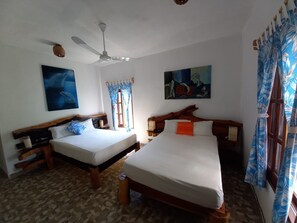 Une chambre avec deux lits simples, un ventilateur de plafond et des œuvres d’art accrochées aux murs.