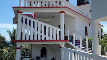 A multi-story building with a white exterior and red accents, featuring a staircase and a red surfboard leaning against the wall.