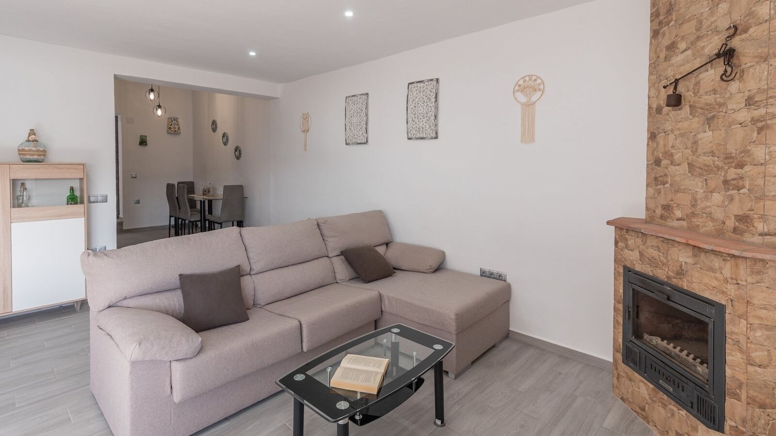 A modern living room with a sectional sofa, a glass coffee table, a fireplace, and a dining area in the background.