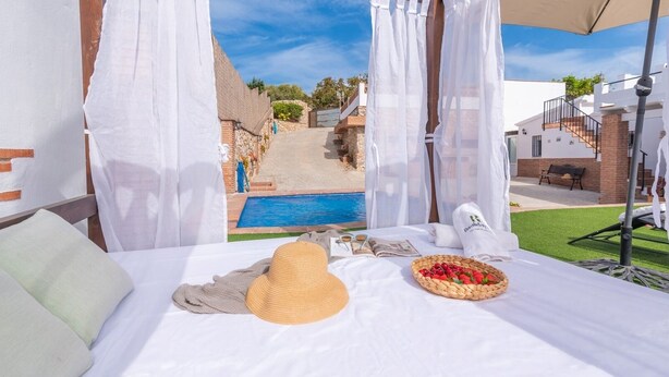 Una cama con vistas a una piscina, cortinas blancas y una cesta de fruta.