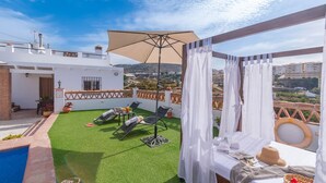 Terraza en la azotea con piscina, sillones de sol, una mesa con bebidas y vistas a la ciudad.