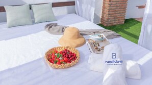 Una cama bien hecha con almohadas, un sombrero de paja, una cesta de fresas y una toalla con un logotipo.