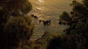 A coastal landscape with a sunset over the sea, surrounded by trees. - Agistri Hotel (Agistri)