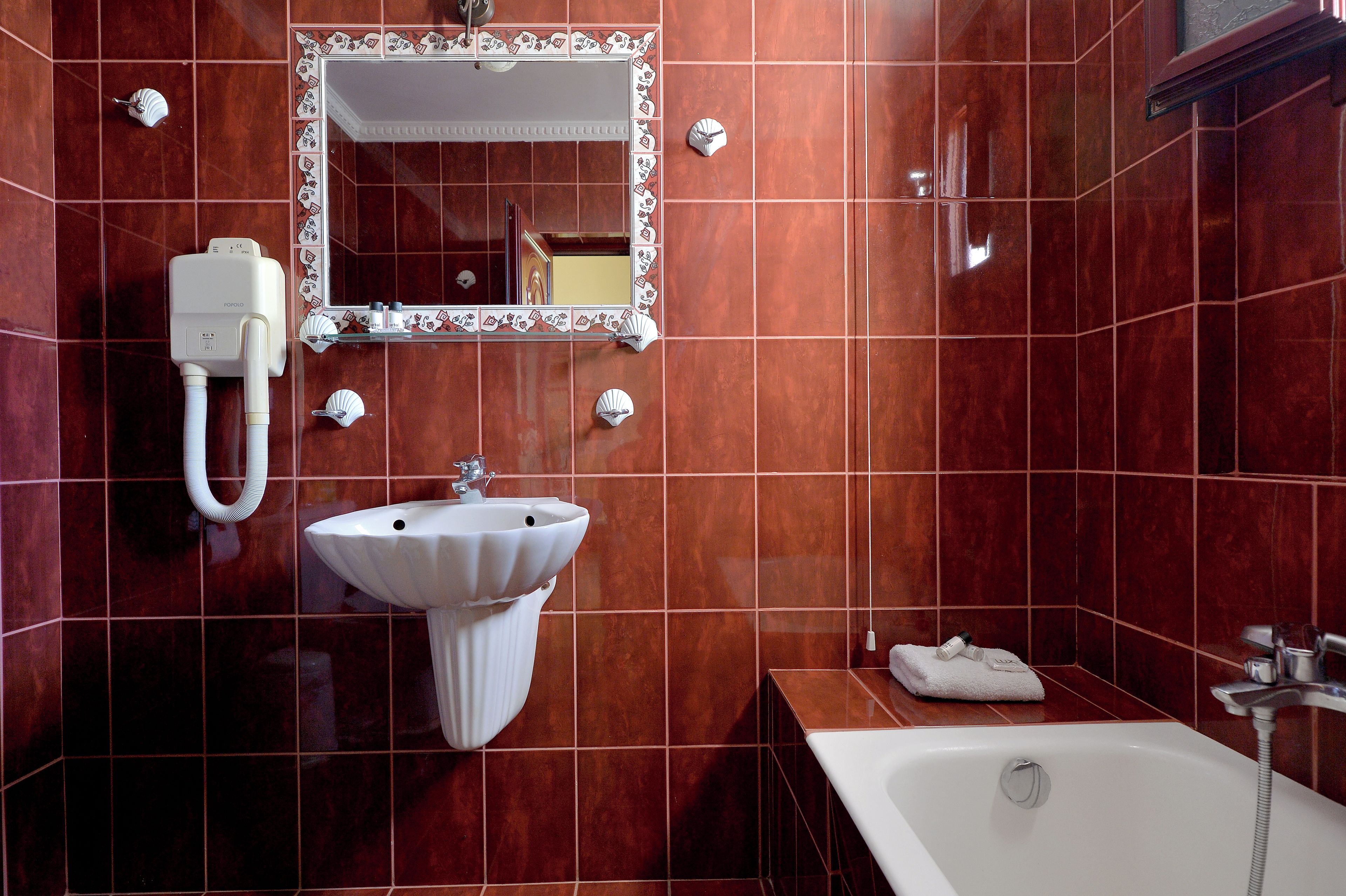 A bathroom with a white sink, a mirror with a decorative frame, a bathtub, and a towel on the side.