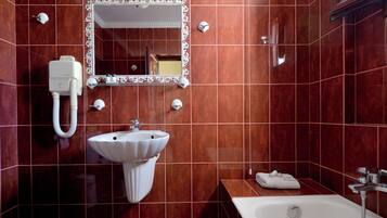 A bathroom with a white sink, a mirror with a decorative frame, a bathtub, and a towel on the side.