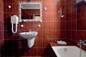 Une salle de bain avec un lavabo blanc, un miroir doté d’un cadre décoratif, une baignoire et une serviette posée sur le bord.