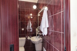 A bathroom with a white toilet, a sink, and a mirror. There is a towel hanging on the wall.