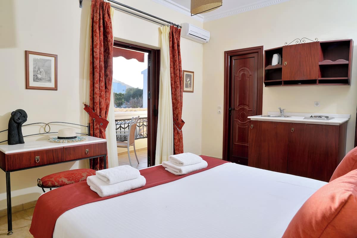 A hotel room with a bed, a desk with a chair, a wardrobe, a bathroom with a sink, and a balcony with a view.