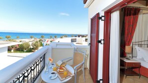 A balcony with a table set for breakfast, a chair, and a bed with a red curtain. - Agistri Hotel (Agistri)