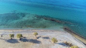 An aerial view of a beach with clear turquoise water, a rocky shoreline, and sparse vegetation.