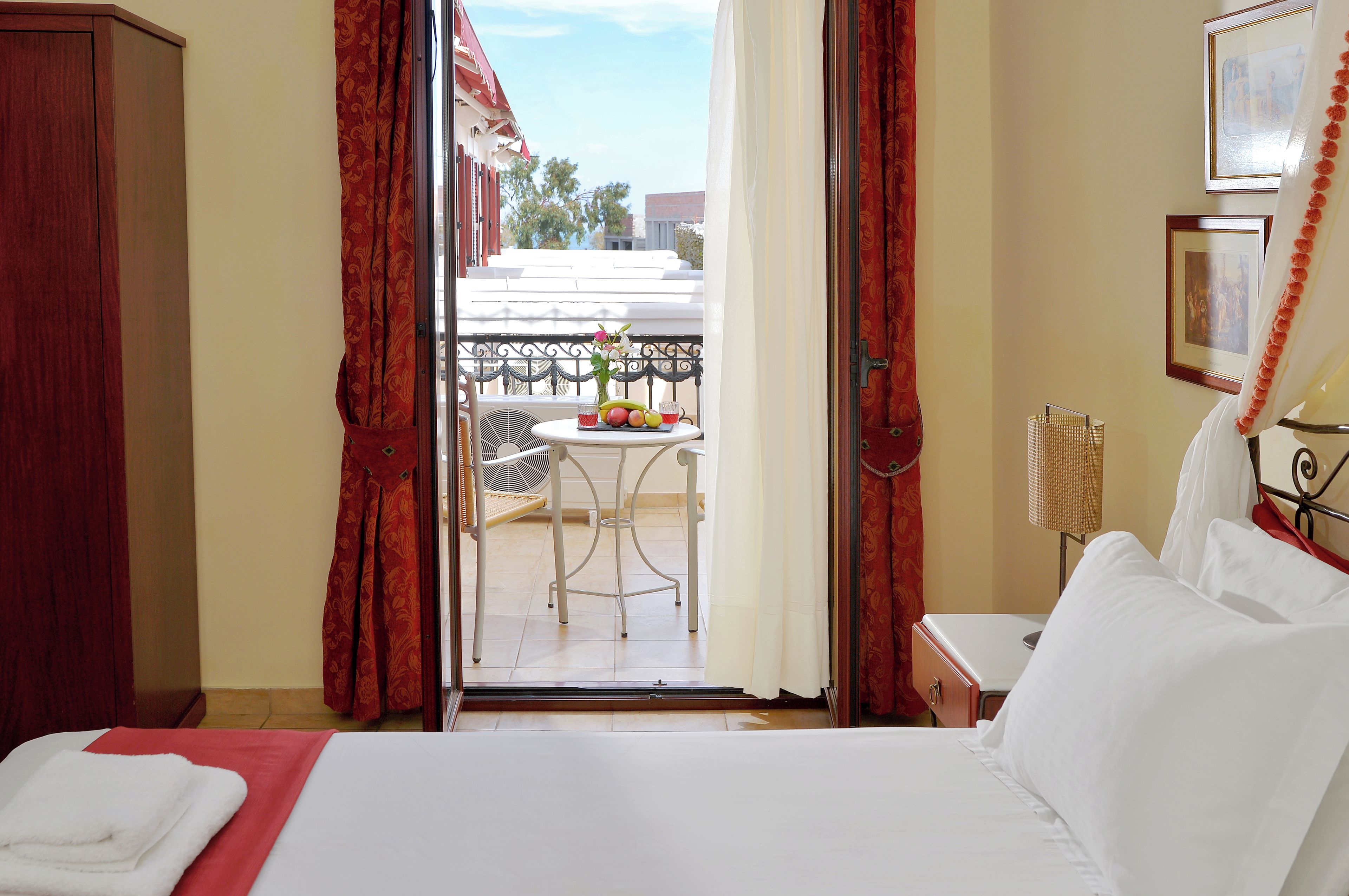 A hotel room with a bed, a small table with fruit, a chair, and a balcony with a view.