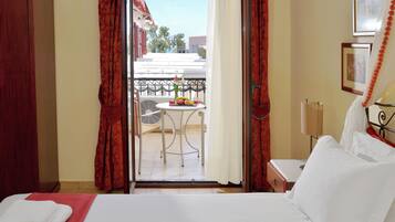 A hotel room with a bed, a small table with fruit, a chair, and a balcony with a view.