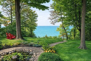 A garden with a pond, red chairs, and a view of the sea.