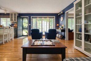 A spacious living room with a wooden coffee table, two blue armchairs, and a view of the outdoors through large windows.