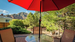 A patio with a glass table and chairs, a red umbrella, and a mountain view. - Agave House, Views Of Chimney Rock, Pets OK! (Sedona)