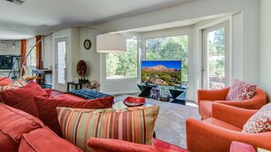 A living room with a large TV, red sofas, and a view of a mountain through the windows. - Agave House, Views Of Chimney Rock, Pets OK! (Sedona)
