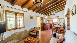 A rustic interior with stone walls, wooden beams, a stone fireplace, a dining area with a table and chairs, and a kitchen with a stove and cabinets. - Villa Noelia Frigiliana by Ruralidays (Málaga)