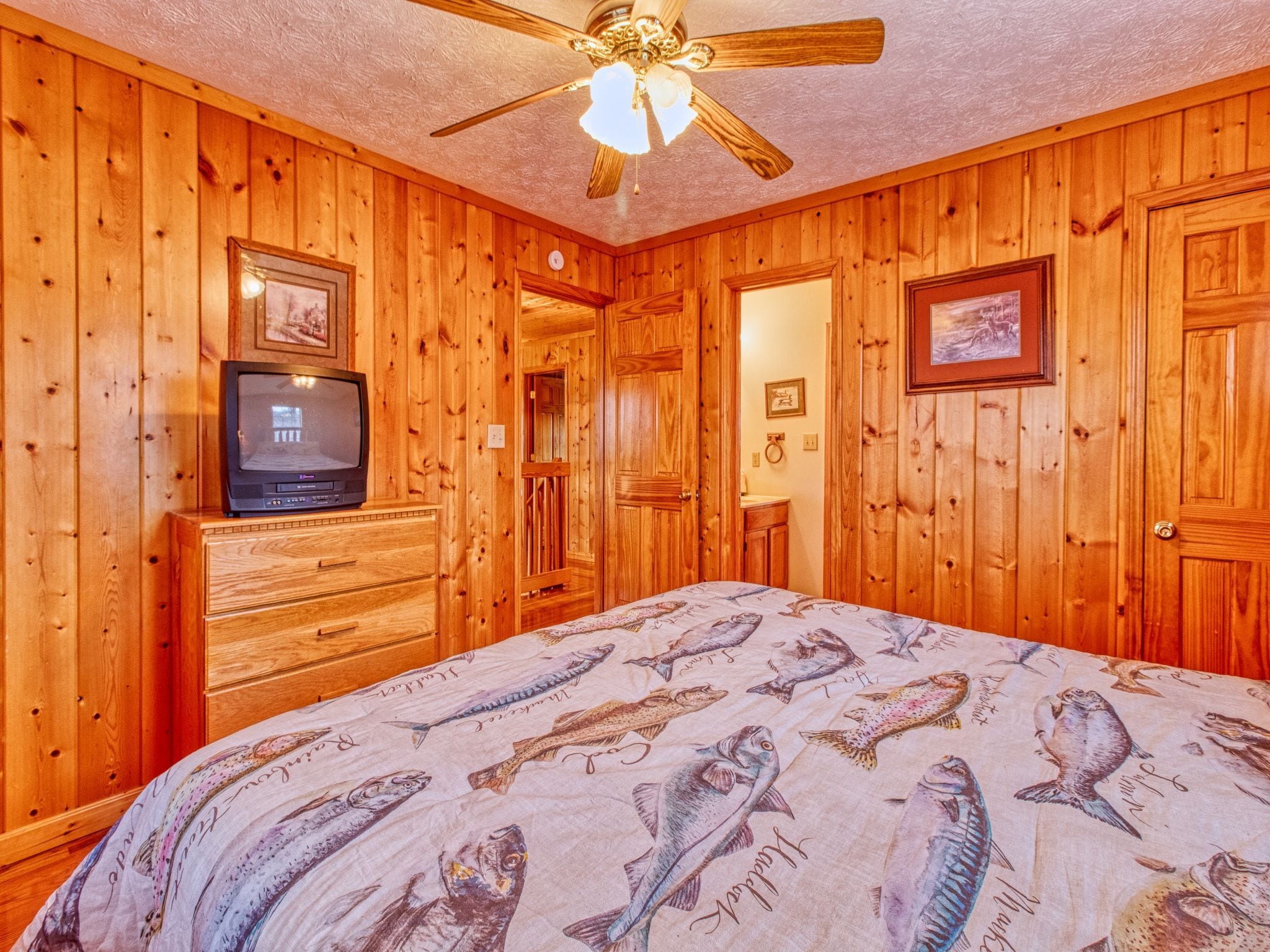 A wooden-paneled room with a bed, a television on a dresser, and a ceiling fan.