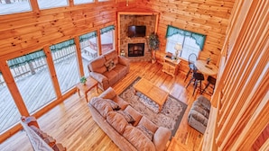 A cozy cabin interior with a stone fireplace, wooden floors, and large windows. - Hawks Point Lodge by Jackson Mountain Rentals (Sevierville)