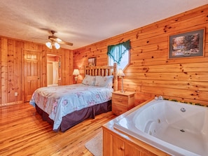 A wooden cabin bedroom with a bed, nightstand, and a large bathtub.
