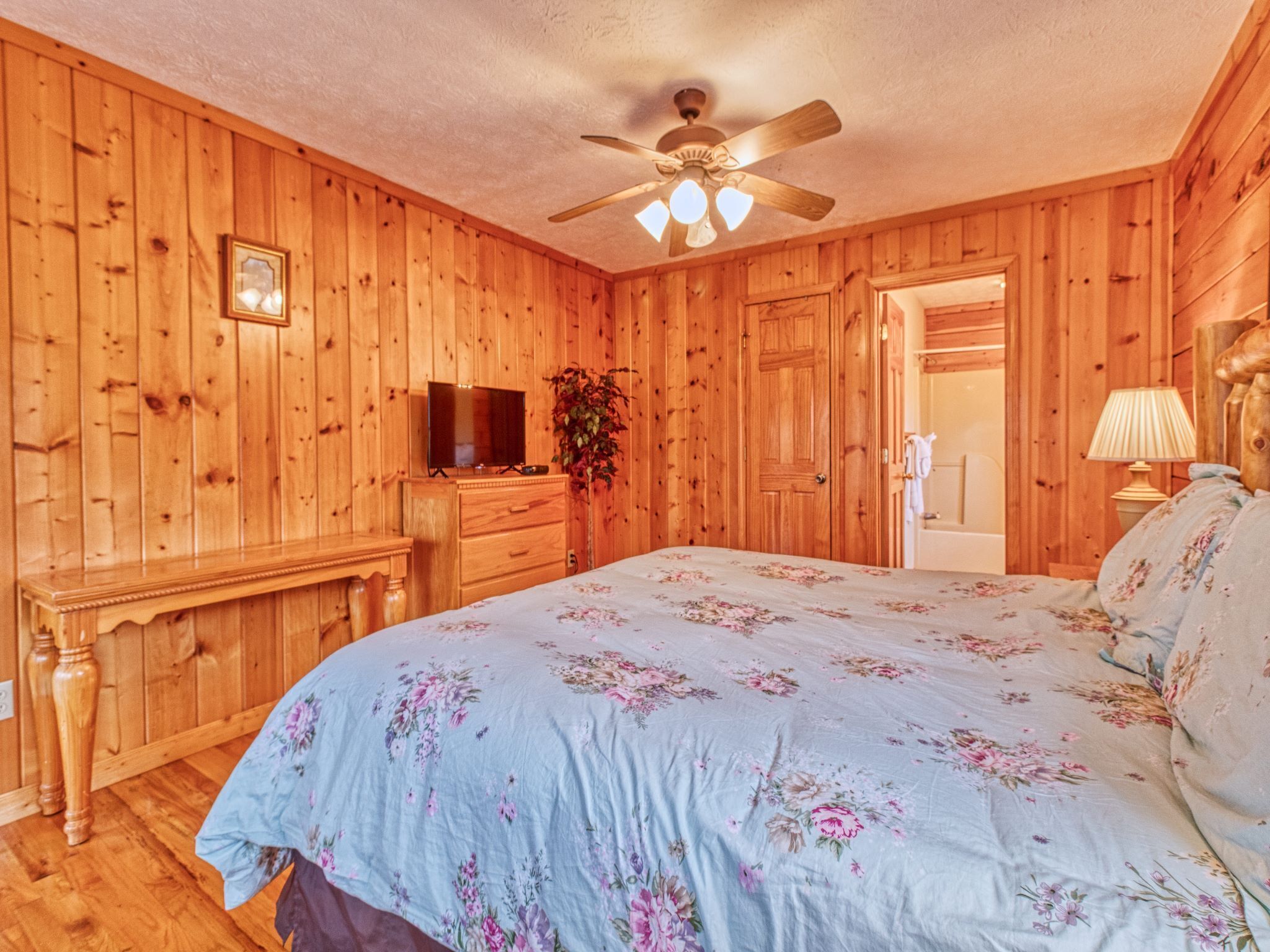 A wooden-paneled room with a bed, dresser, television, and a ceiling fan.