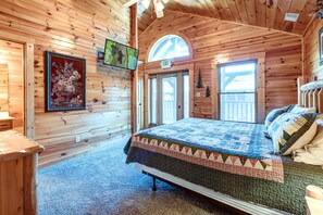 Une chambre dans un chalet en bois, équipée d’un lit, d’une télévision et d’un tableau représentant des fleurs, encadré.