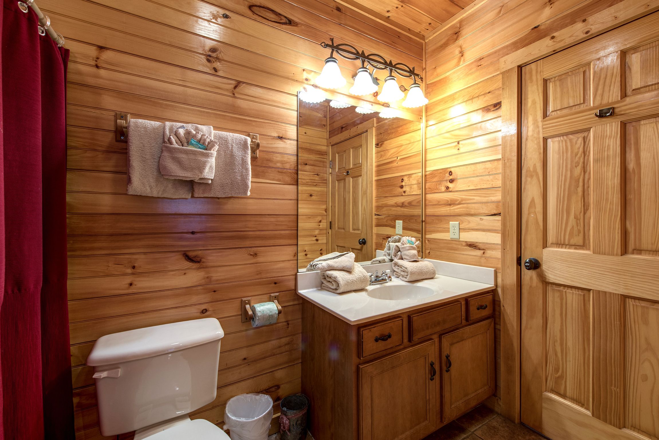 A wooden cabin bathroom with a toilet, sink, and mirror.