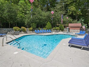 A swimming pool with blue lounge chairs and a stone wall. - Highpoint Escape by Jackson Mountain Rentals (Gatlinburg)