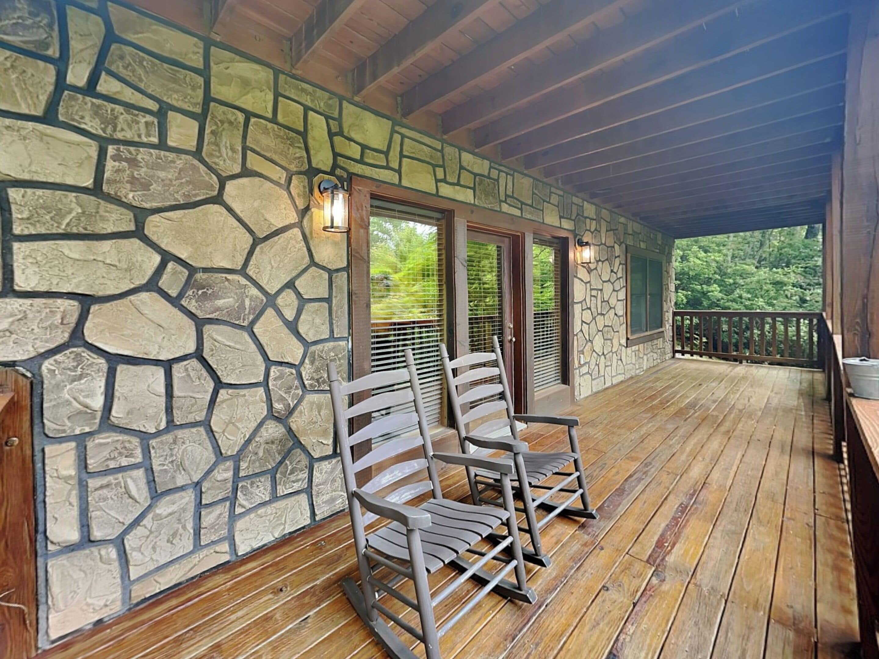 Eine überdachte Veranda mit Steinwänden, Holzboden und zwei Schaukelstühlen.