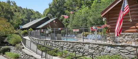 A wooden cabin with a stone retaining wall, a pool area, and an American flag.