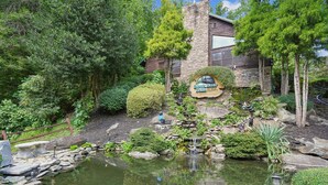 A landscaped garden with a pond, stone walls, and a wooden cabin labeled 'Black Bear Falls.' - Highpoint Escape by Jackson Mountain Rentals (Gatlinburg)