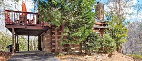 A cabin with a covered porch, a stone chimney, and a forested backdrop.