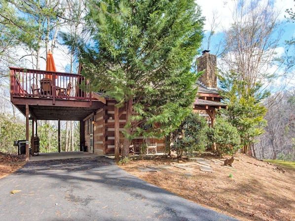 A cabin with a covered porch, a stone chimney, and a forested backdrop. - Fox Den by Jackson Mountain Rentals (Gatlinburg)