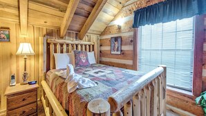 Ein Schlafzimmer einer Holzhütte mit Bett, Nachttisch, Lampe und einem Fenster mit Jalousien.