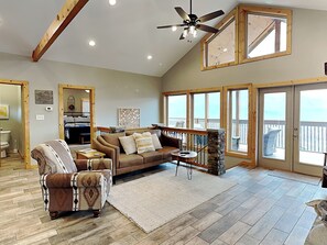 A spacious living room with a high ceiling, a ceiling fan, and large windows offering a view of the outdoors. - Hello Smokys by Jackson Mountain Rentals (Gatlinburg)