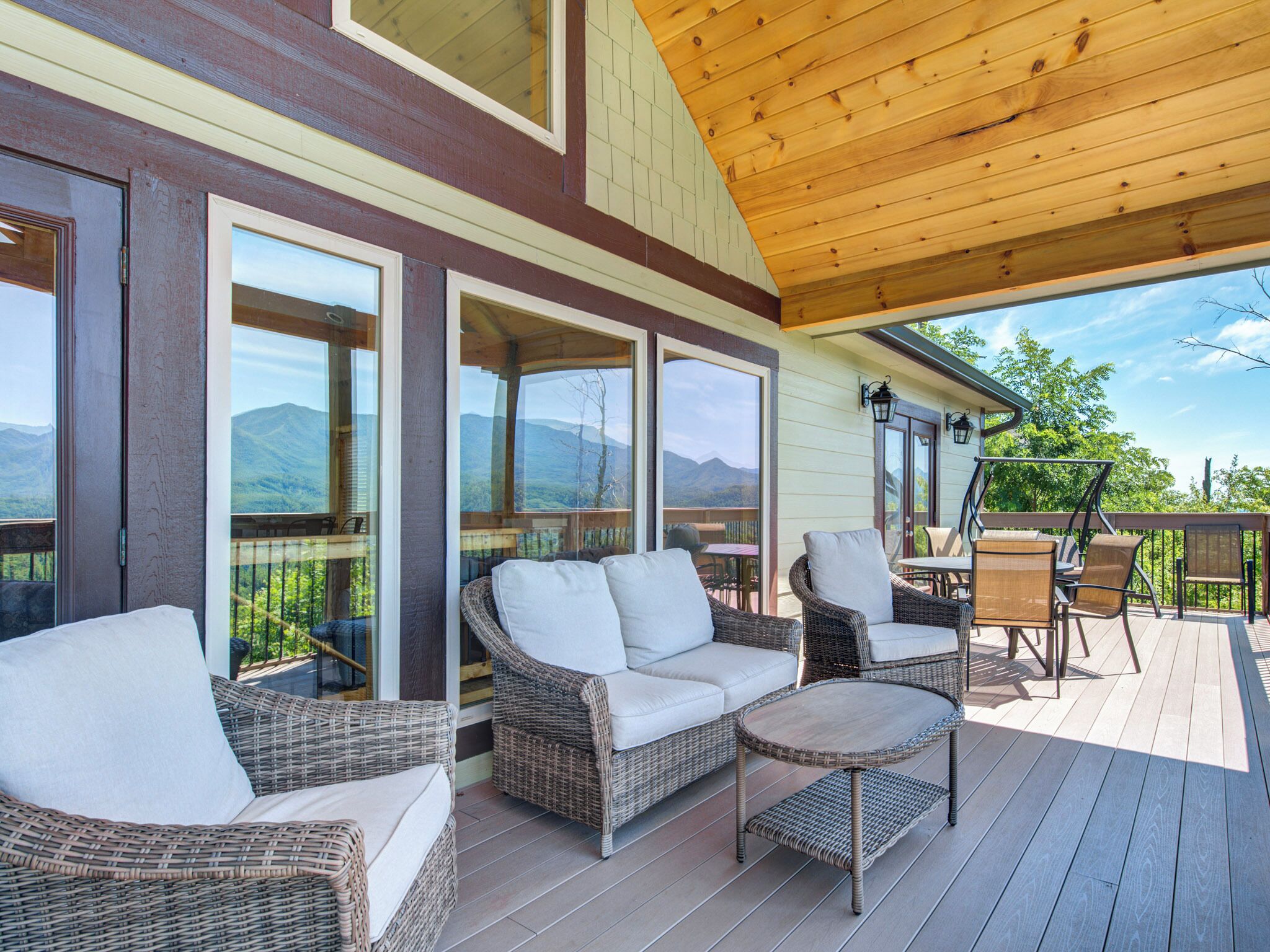 A covered outdoor deck with wicker furniture and a table, overlooking a mountainous landscape.