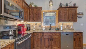A kitchen with wooden cabinets, stainless steel appliances, a coffee maker, and a clock on the wall.