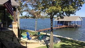 A lakeside deck with a covered seating area, a dock, and a flag. - Beautiful gated lakefront home built im 2020 (Mabank)