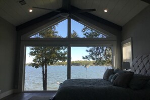 Ein Schlafzimmer mit großem Fenster mit Seeblick, einem Bett mit vielen Kissen und einem Deckenventilator.