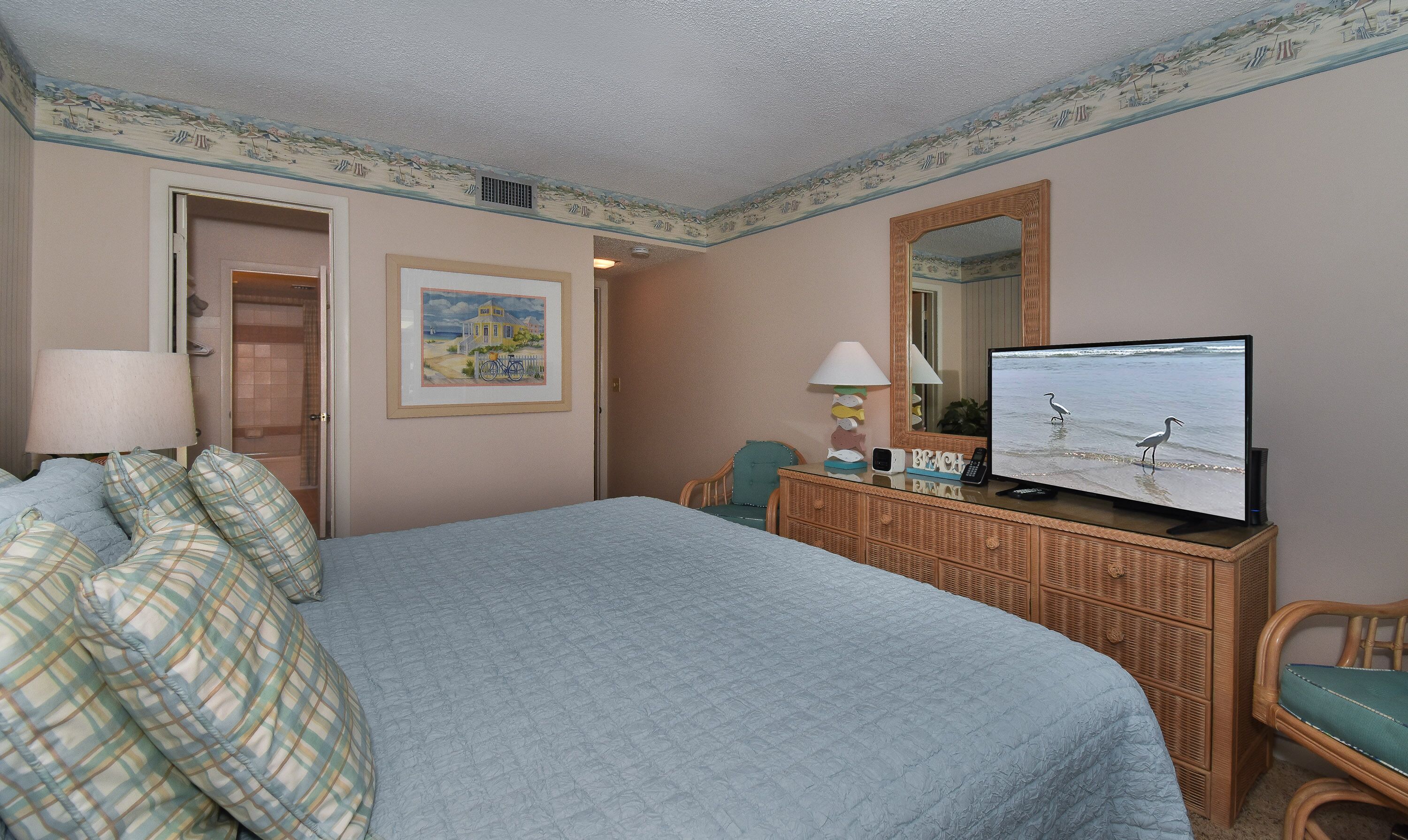 Ein Hotelzimmer mit einem großen Bett, einem Fernseher, einem Schminktisch und einer Tür zu einem weiteren Raum.