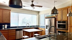 Une cuisine moderne avec des meubles en bois, un réfrigérateur en acier inoxydable, un four, un évier et un ventilateur de plafond.